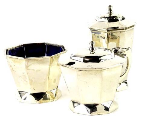 An Edward VIII silver three piece Art Deco cruet, comprising mustard pot, open salt and pepper pot, with blue glass liners, Birmingham 1936.