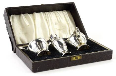 A George VI silver three piece cruet, in the Art Deco style, comprising salt, pepper pot, mustard, with two spoons, Birmingham 1946, in a fitted case.