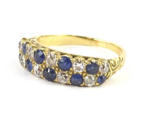 A sapphire and diamond ring, with two row design of round brilliant cut stones, each in claw setting, alternating stones, with scroll design shoulders, yellow metal, unmarked, ring size O, 4.1g all in.