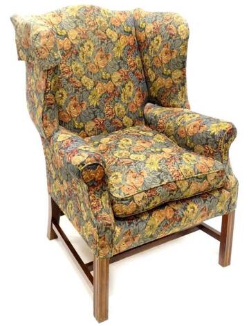 A mahogany wingback chair, in George III style upholstered in floral fabric, on channelled legs with H stretcher. The upholstery in this lot does not comply with the 1988 (Fire & Fire Furnishing) Regulations, unless sold to a known exporter or upholstere