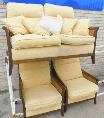 A Parker Knoll bergere three piece suite, with stained beech frame, upholstered in patterned gold coloured fabric.