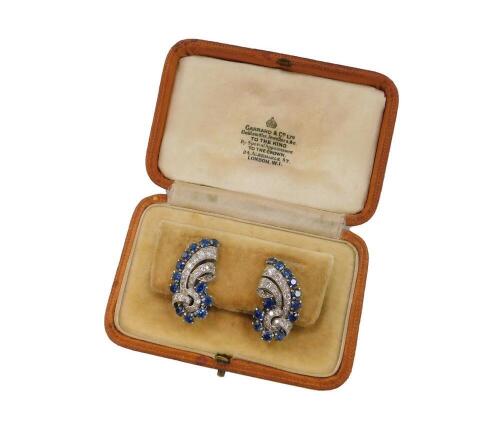 A pair of Garrard & Company mid 20thC sapphire and diamond ear or lapel clips, of scrolling form set in white metal, engraved Garrard London, cased, 14.3g all in.