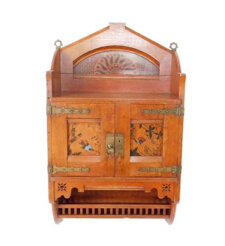 A Victorian Aesthetic period oak wall cabinet, c1880s, the three sided shelf top painted to the back with a sunburst motif, above two doors, with ornate brass hinges and door plates, having central panels painted with exotic birds, above a single gallerie