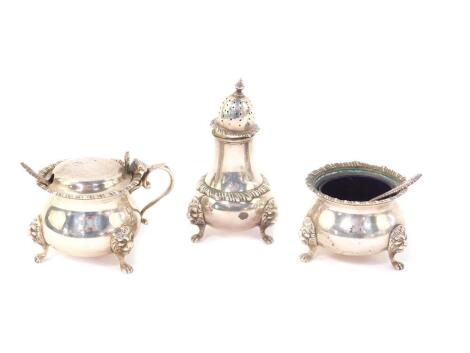 A silver three piece condiment set, with gadrooned rims, raised on three lion's paw and mask feet, with blue glass liners, comprising mustard pot and spoon, salt cellar and spoon, and a pepperette, London 1958, 10.80oz.