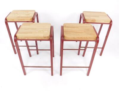 A set of four burgundy metal laboratory stools, with oak seats and metal cross bars, each 64cm H.