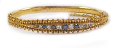 A Victorian 15ct gold sapphire and diamond bangle, channel set on a snap clasp with safety chain as fitted, presentation engraved internally, Birmingham 1886, 11.8g all in.