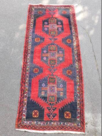 A Hamadan runner, with a central multi coloured pole medallion on a red and blue ground, with multiple borders, 305cm x 125cm.