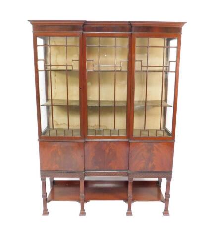 An Edwardian Chinese Chippendale style flame mahogany break front display cabinet, the outswept pediment over two drawers, flanking a further glazed panel enclosing two shelves, above two cupboards raised on fluted supports united by a shaped under tier, 