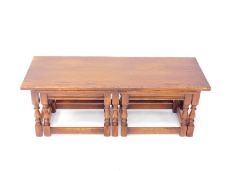 A Reprodux oak nest of tables, comprising one long table and two small slot in tables, raised on turned legs, united by stretchers, long table 41cm H, 115.5cm W, 44cm D, short table 38cm H, 47.5cm W, 37.5cm D.