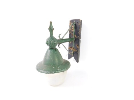 A green painted metal wall hanging street lamp, circa 1920s, with a plastic bucket shade, wooden mounted, 48cm H, 39cm W.