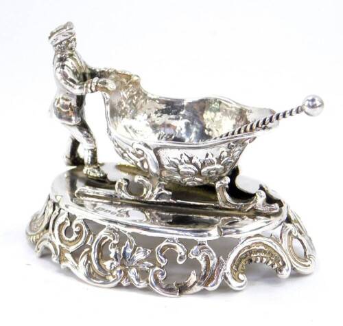 A continental late 19thC silver novelty salt, modelled as a man pushing a troika, embossed with flowers, raised on an oval base pierced and embossed with rococo scrolls and leaves, import marks, William Moering, London 1896, together with a silver salt sp