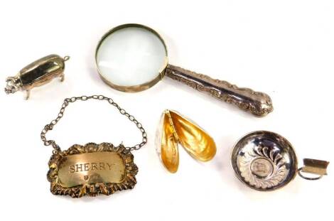 A pair of silver moules eaters, formed as a mussel shell, Birmingham 1998, silver sherry label, London 1972, silver figure of a pig, silver individual ashtray, London 1998, 2.11oz, and a magnifying glass with a silver handle, Sheffield 1900.