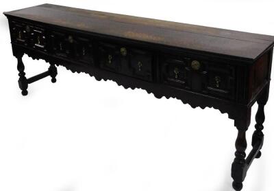 An 18thC oak dresser base, the rectangular plank top with the moulded edge above four panel drawers each with pierced brass escutcheons and tear drop handles with a shaped apron on turned supports with end stretchers and bun feet, 207cm W, 45cm D.