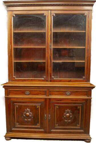 A late Victorian walnut cabinet bookcase, with egg and dart moulded cornice over two moulded and glazed doors revealing adjustable shelves, over two frieze drawers with oval pressed brass ring handles, and two panelled doors with applied and carved cartou