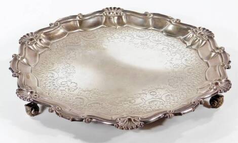 An Edward VII silver pie crust salver, engraved with flowers and rococo scrolls, raised on three scroll feet, London 1902, 29.22oz.