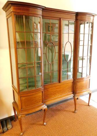 An Edwardian mahogany inverted breakfront china cabinet, with a moulded top raised above a pair of central astragal glazed doors, flanked by a pair of curved astragal glazed panels, above an arrangement of three cupboards on cabriole legs terminating in c