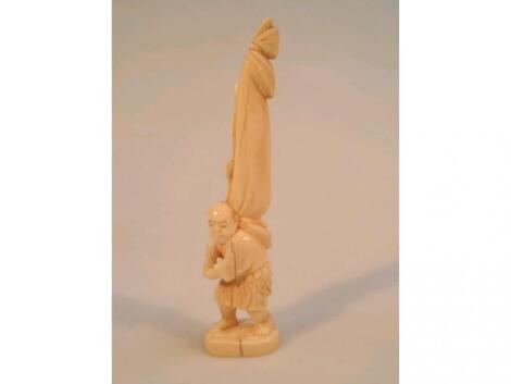 A Japanese carved ivory standing figure of a man holding a folded tent