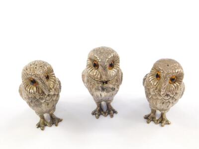 A three piece silver novelty owl condiment set, each standing owl inset with glass eyes, comprising salt, pepperette, and mustard pot with a spoon with mouse terminal, Richard Comyns, London 1975, 11.14oz. - 2