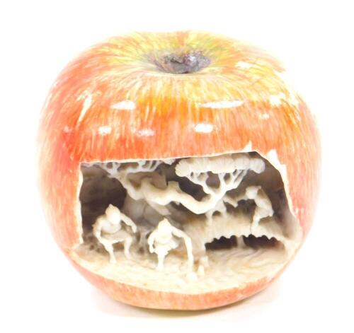 A Chinese 19thC ivory carving of an apple, the front open and showing figures and trees internally, exterior over painted in apple flesh tones, 5.5cm Dia.