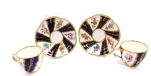 A pair of late 18thC Sevres coffee cups and saucers, of ogee form, decorated with reserves of flowers, and foliate gilding, against a bleu de roi ground, painted marks.