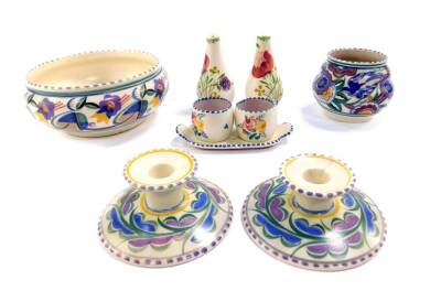 A group of Poole Pottery, traditionally painted with flowers, comprising a pair of candlesticks, bowl, ogee shaped vase, and two egg cups on a stand, together with a salt and pepper. (9)