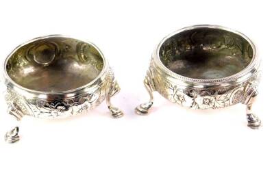 A pair of Georgian matched silver circular salts, embossed with flowers, raised on three cabriole legs and hoof feet, hallmarks indistinct, 2.55oz.