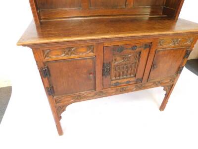 A Victorian oak dresser, the outswept pediment over a two shelf plate rack, above three carved doors, centre door with iron strap work raised on square legs, 208cm H, 126.5cm W, 55.5cm D. - 4