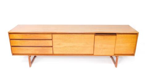 A late 20thC teak sideboard by White & Newton Ltd Portsmouth, the central fall flap flanked by three long drawers to the left, two cupboard doors to the right, raised on rectangular supports united by a stretcher, 69.5cm H, 217cm W, 44cm D.