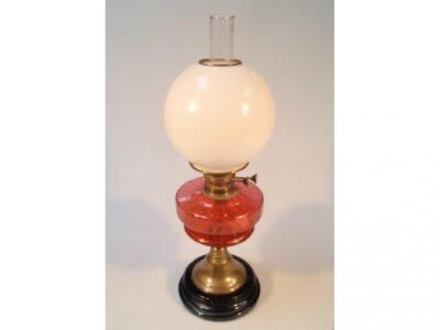 A Victorian oil lamp with a cranberry glass reservoir on a brass column