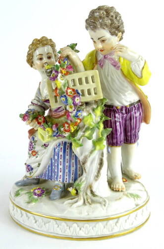 A late Meissen porcelain figure group, comprising a young boy and a girl beside a rectangular cage, holding garlands of flowers etc., on an oval base, blue cross sword marks to underside, incised number 61264 and impressed number 29X, 12cm W.