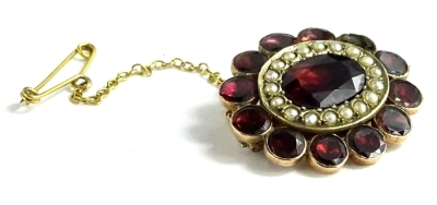 A Victorian garnet and seed pearl cluster brooch, lacking one garnet, with central garnet surrounded by seed pearls and garnet petals to border, with safety chain, 3.8g all in, 2.5cm W.