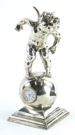 A silver coloured metal mantel clock, cast in the form of a putto on a globe, the movement stamped Quartz, on a square base, 21cm H.