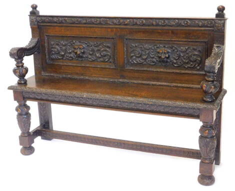 A late Victorian carved oak settle, decorated with leaves, scrolls, flowers and masks, on turned feet, 124cm W.