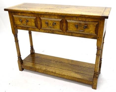 An oak side table, the triple planked top with cleted ends, above three frieze drawers, on turned supports with pot board base, possibly Titchmarsh and Goodwin. 99cm W, 35.5cm D, 76.5cm H.