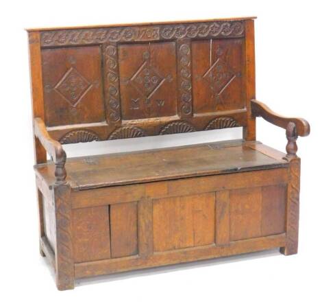 An oak settle, the raised panelled back carved with initials M W and bearing date 1703, the base with a hinged seat and shaped arms above panelled front and sides, constructed from old timber, 116cm W.