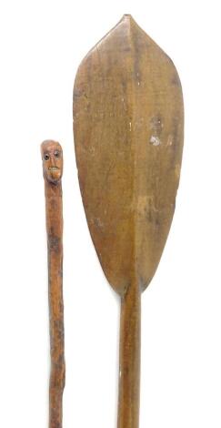 A tribal paddle of plain form, with turned handle and shaped finial, 110cm L, and a tribal walking stick carved with a mask. (2)