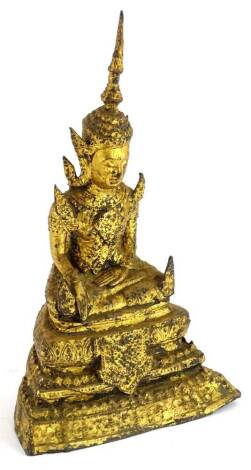 A gilt metal Indian figure of a seated god, with legs crossed on a stepped base, dressed in finery, 20cm H.