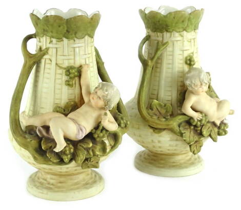 A pair of Royal Dux porcelain vases, each decorated with stylised basket weave, mounted with a putto seated on grapes and vines, printed mark and pink triangle mark to underside, 23cm H.