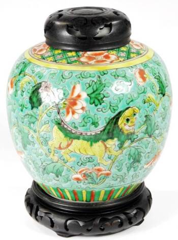 A 19thC Chinese porcelain ginger jar, with carved wooden cover, raised with a geometric and floral upper border, the main body decorated with exotic animals on a green ground, polychrome decorated, on a wooden stand, 27cm H.