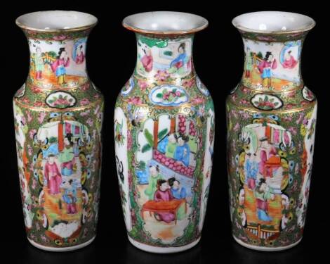 A pair of Cantonese famille rose vases, each with squat trumpet stems, decorated with panels of figures in an interior scene, broken by further panels of birds and flowers, predominately in pink, green and blue, on circular feet, and another vase similar,