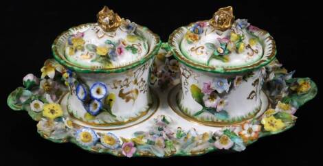 A 19thC Coalbrookdale porcelain inkstand, the shaped plate and two inkwells heavily encrusted with flowerheads and foliage, with gilt highlights predominately in blue, yellow and green, the stand with an outer floral banding, on shaped foot, unmarked, 22c