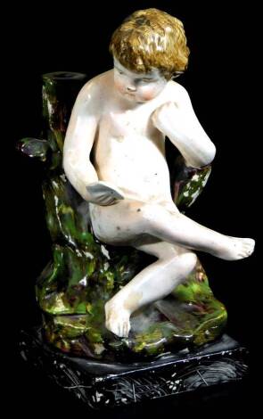 An early 19thC Creamware pottery figure of a cherub, aside tree bough, polychrome decorated, predominantly in cream, green and brown, 20cm H.