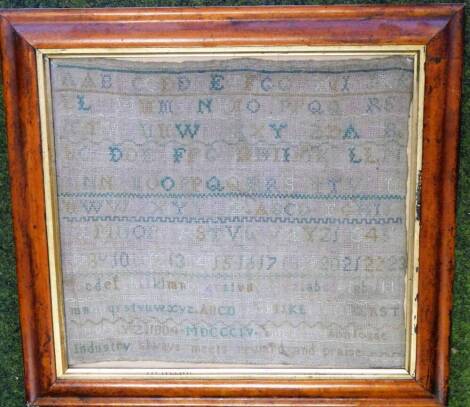 A 19thC needlework sampler, with lines of alphabetical and numerical samples and motto Industry always meets reward and praise, 32cm x 35cm, in maple frame.