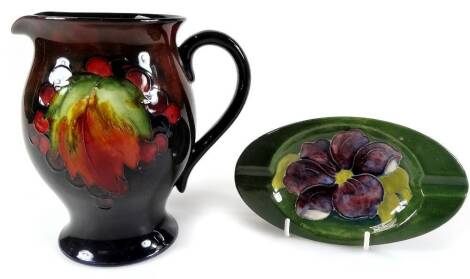 A 20thC Moorcroft flambé leaf and berry pattern jug, the bulbous body with plain spout and handle, on circular foot, impressed marks beneath, 16cm H, and a Moorcroft ashtray. (2)