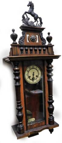 A early 20thC walnut cased Vienna wall clock, surmounted with horse finial, on a pierced and scroll plinth flanked by urns, above a glazed case flanked by quarter columns, heavily carved, with 13cm Dia. Arabic dial, pendulum swung 8-day movement, 98cm H.