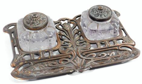 An early 20thC Art Nouveau ink stand, set with two glass bottles, on an entwined lotus flower and scroll stand, partially pierced with spaces for pens to the front, registered number beneath, 26cm W.