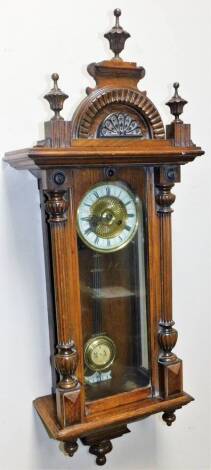 An early 20thC oak cased Vienna wall clock, the cornice with three urn finials, above a carved floral patera, a heavily carved glazed case flanked by quarter columns, with 15cm Dia. Roman numeric dial revealing a 8-day keywind movement, 100cm H.