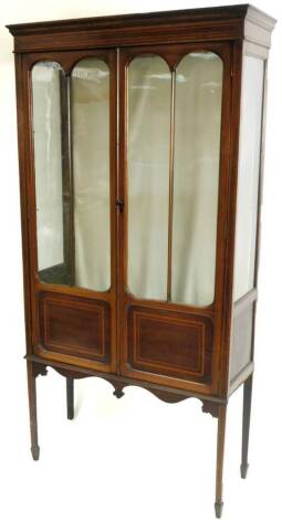 An Edwardian mahogany and boxwood strung display cabinet, the moulded top raised above a pair of arched doors with panels beneath, on square tapering legs terminating in spade feet, 171cm H, 85cm W, 30cm D. (AF)