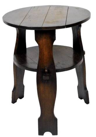 An Arts and Crafts type oak cricket table, the circular plank top raised above shaped stiles, joined by a shelf, 69cm H, 56cm Dia.