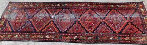 A Persian runner, with a design of five lozenges on a red ground with three borders, 100cm x 294cm. (AF)